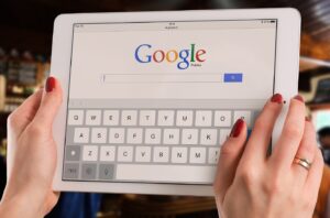 A tablet being held by female hands with the google search home page displayed.